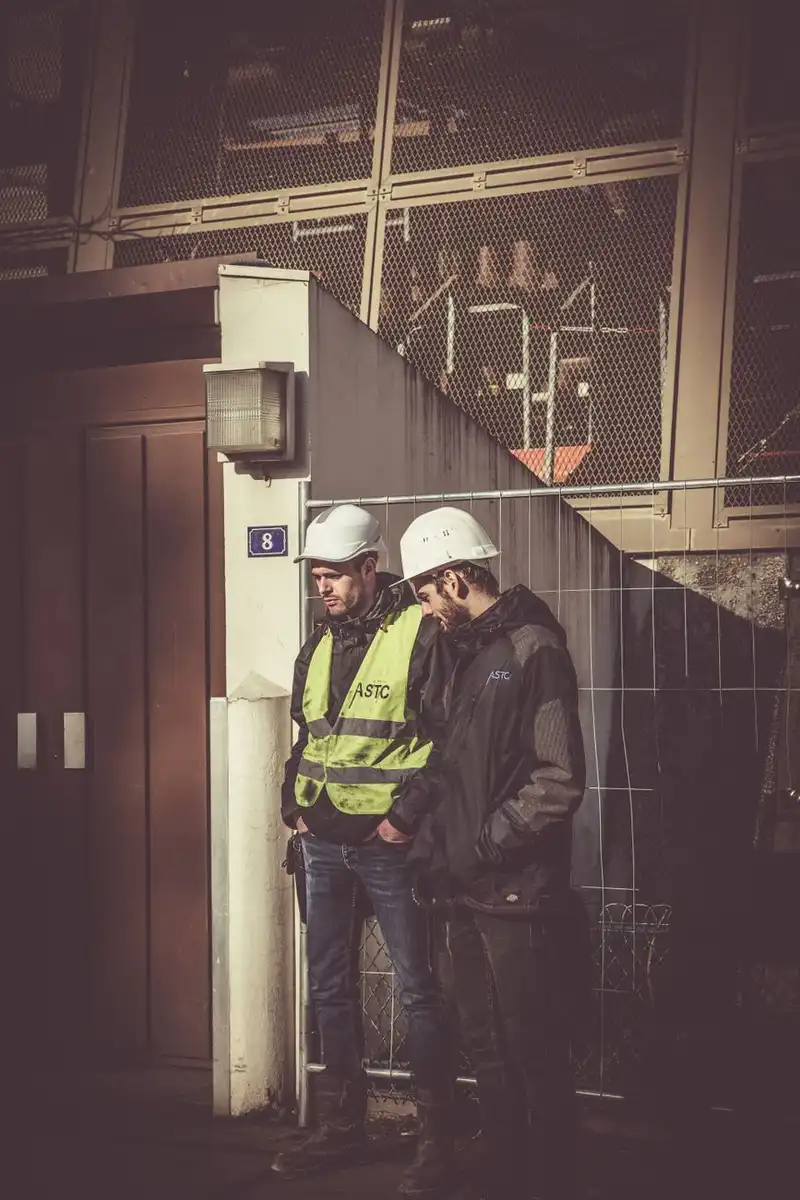 Dois trabalhadores com capacete e uniforme de segurança em um canteiro de obras